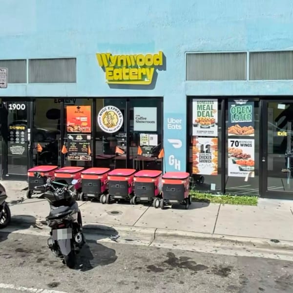 Wynwood Eatery storefront with delivery robots, a scooter, and promotional signs for food deals.