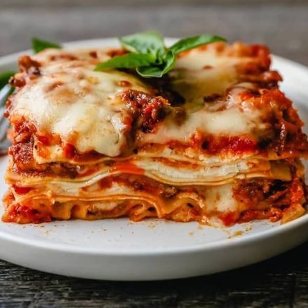 A delicious slice of lasagna with melted cheese and basil on a white plate.