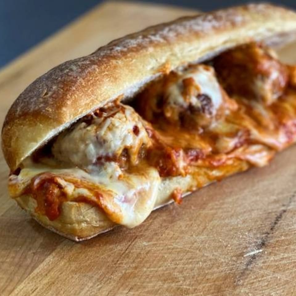 A meatball sub sandwich with melted cheese and marinara sauce on a wooden cutting board.